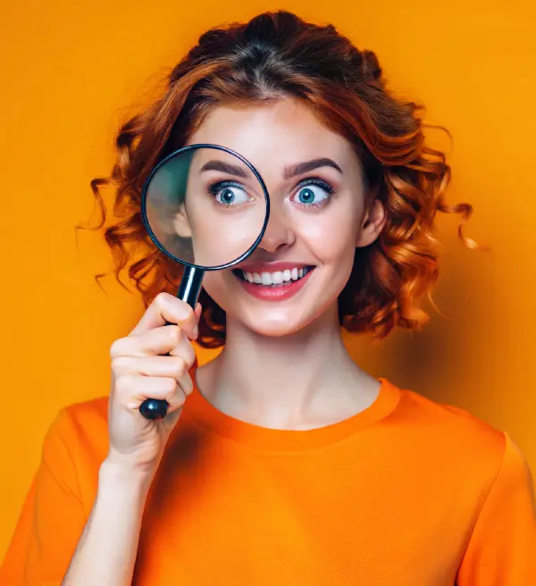 Jeune femme sur fond orange regardant à travers une loupe